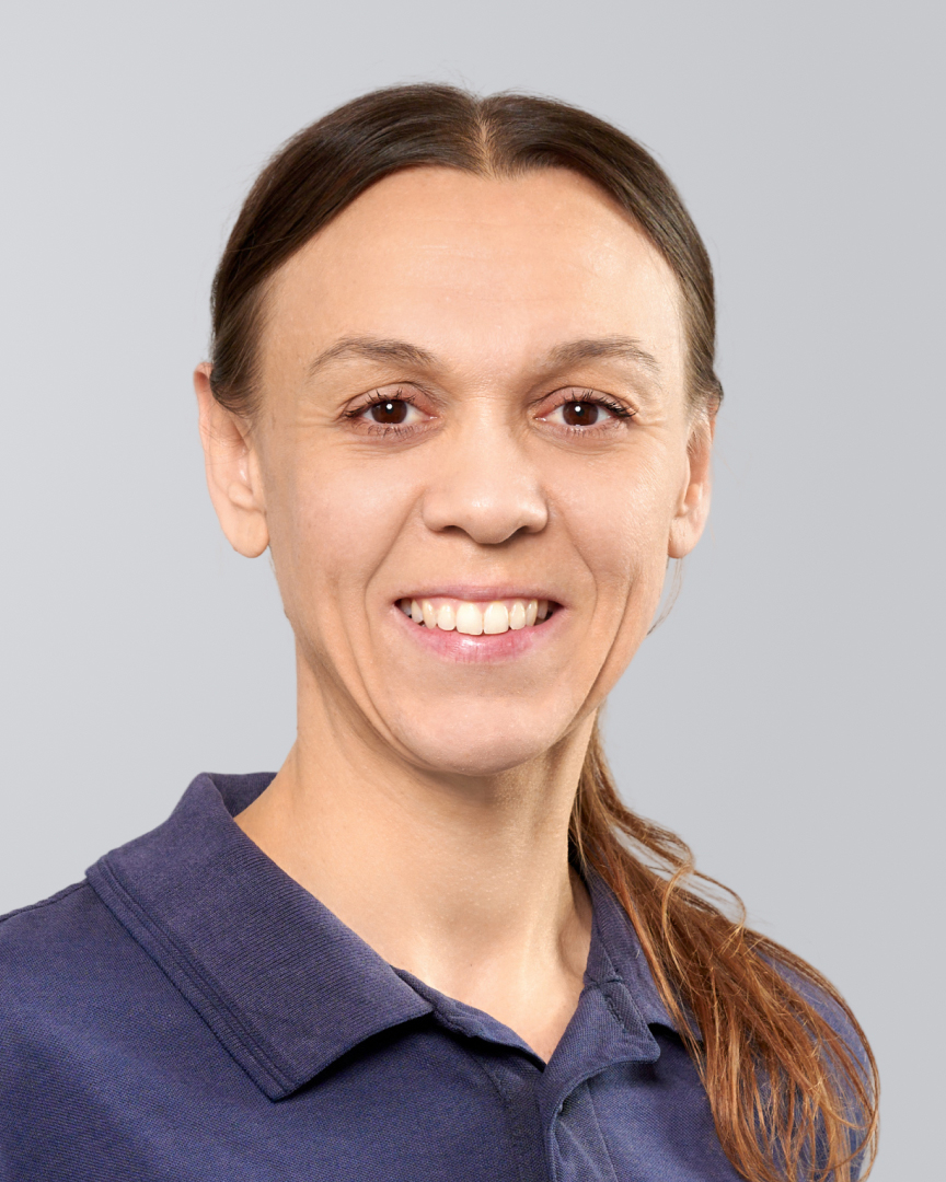 Porträt einer Frau mit langen, glatten Haaren und blauem Poloshirt vor einem neutralen Hintergrund.