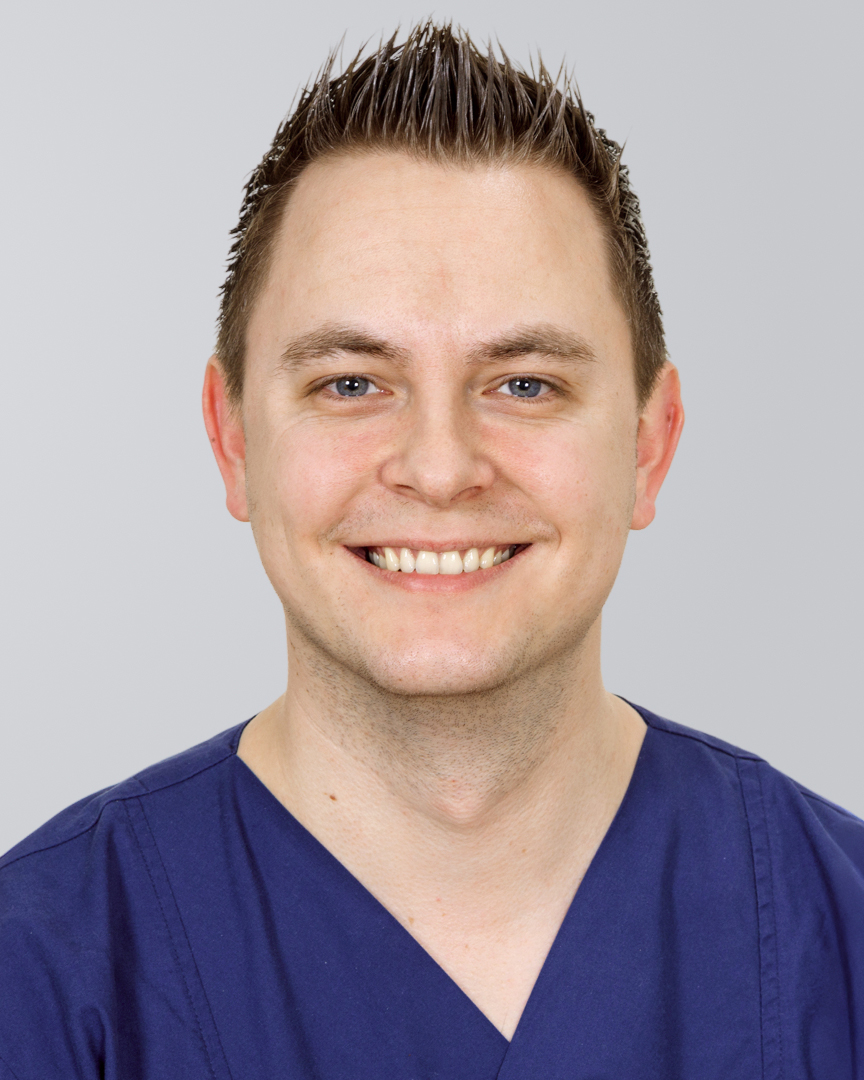 Lächelnder Mann in blauer Arbeitskleidung vor einem grauen Hintergrund.